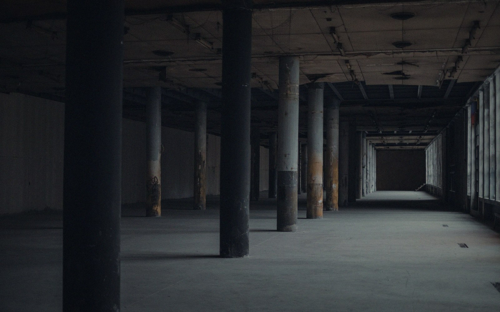 An empty club floor at early morning, light entering from a high window across a concrete surface, abandoned cups at the edge