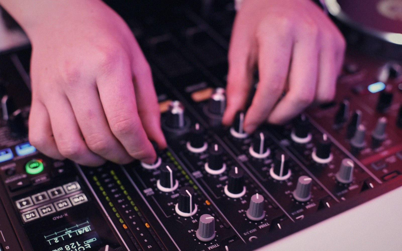 Close-up of hands adjusting knobs and sliders on a DJ mixing console