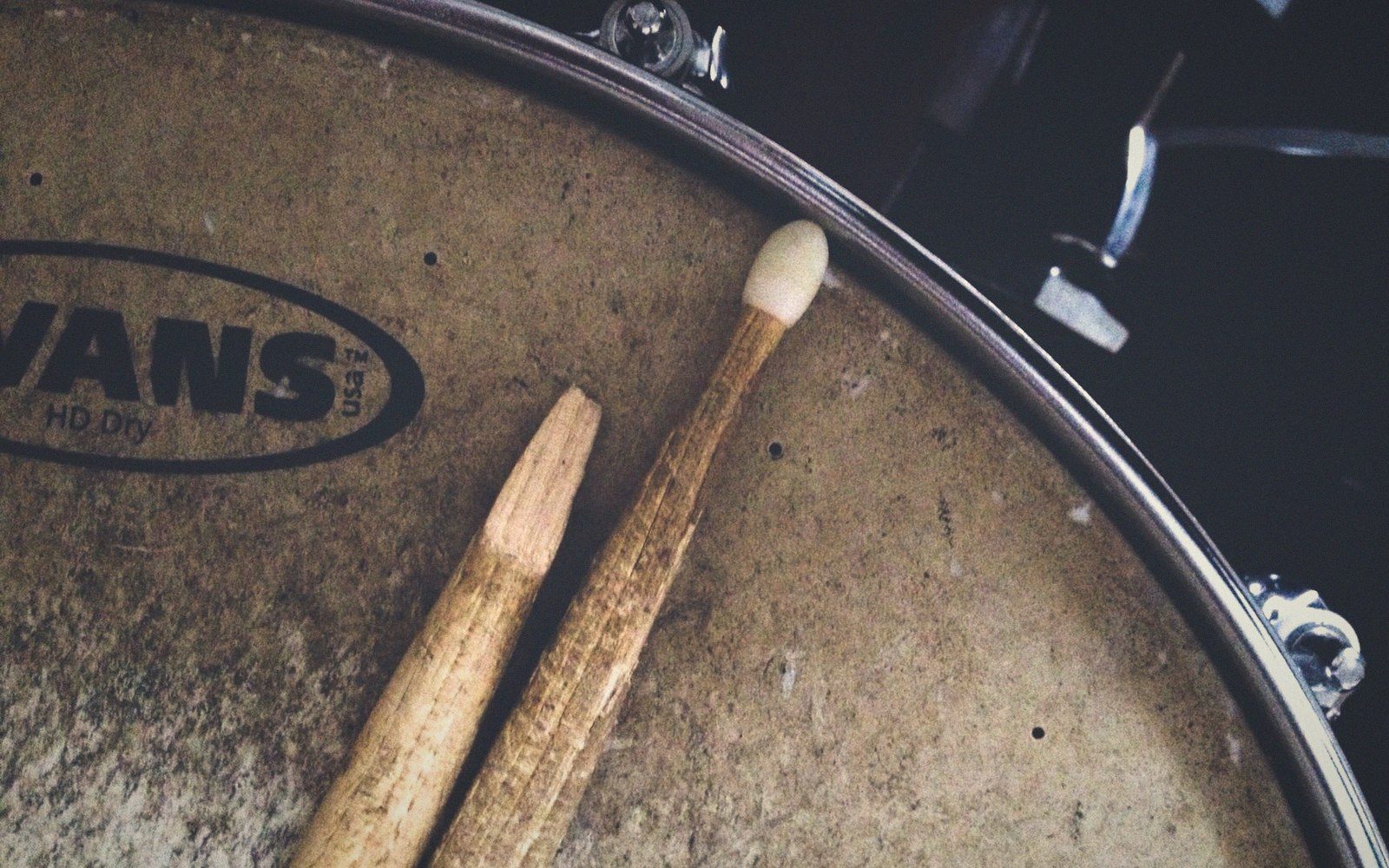 Two wooden drumsticks resting on a worn snare drum head with Evans branding