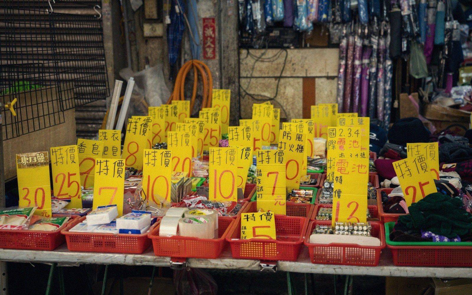 Yellow price signs with Chinese characters mark discounted goods in red baskets at a market stall