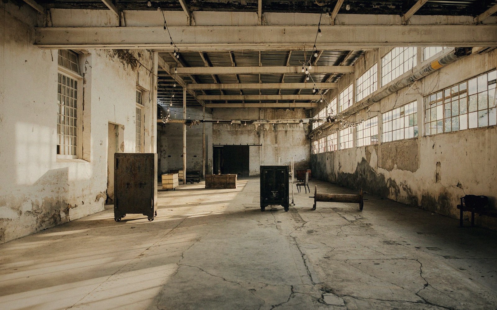 Empty industrial warehouse with peeling walls, large windows, and scattered old furniture
