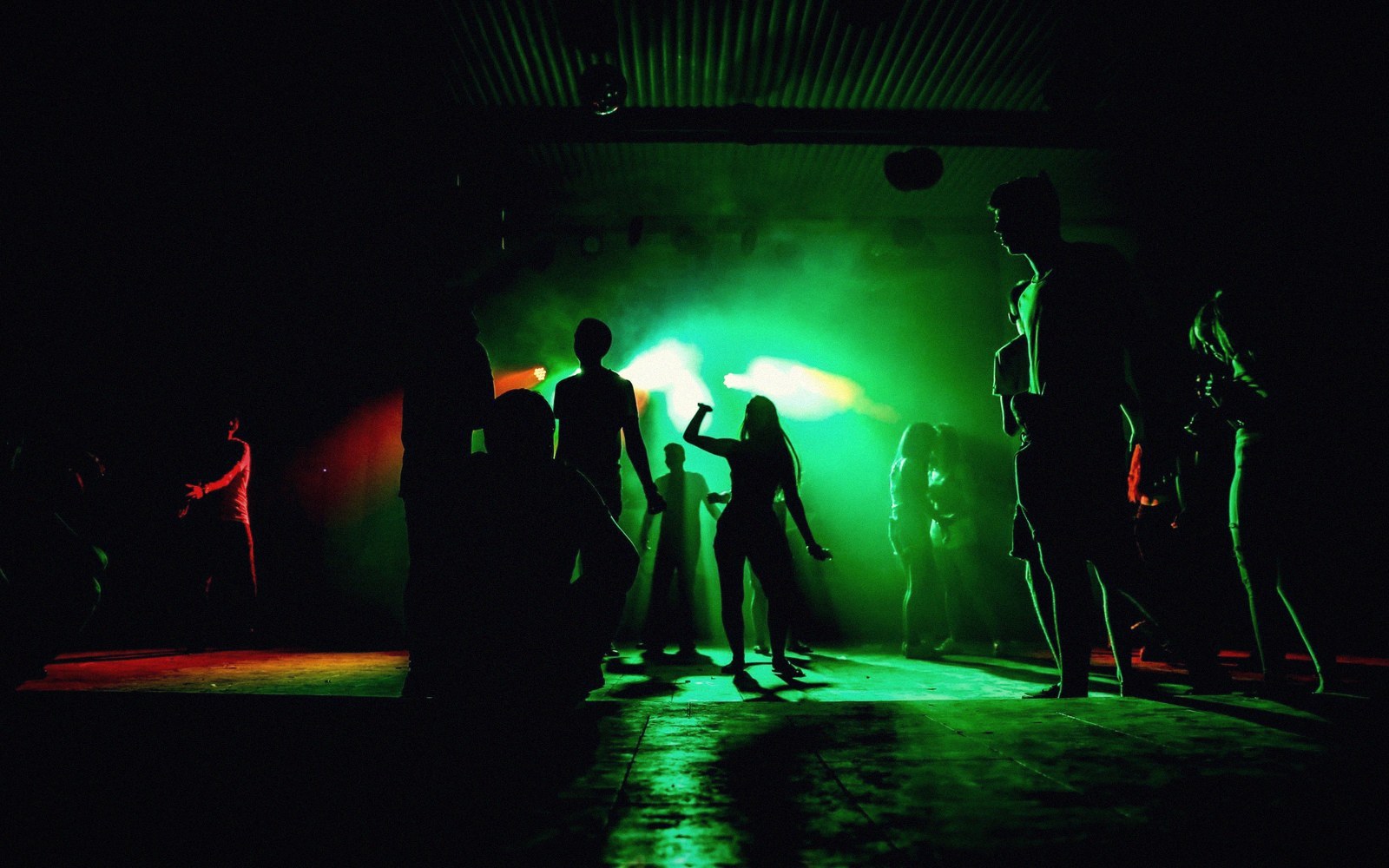 Silhouetted dancers move under green stage lighting in a smoky nightclub
