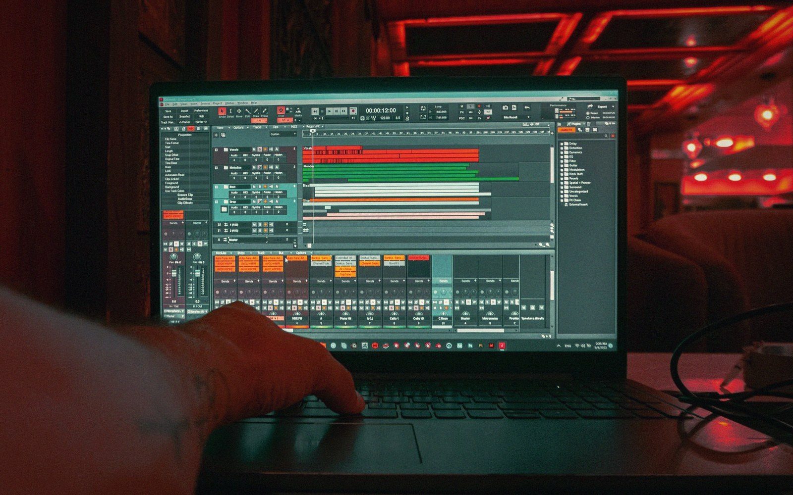 A hand on a laptop trackpad edits audio tracks in a music production program